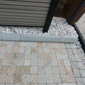 Paved area with stone tiles and gravel, featuring a building structure.