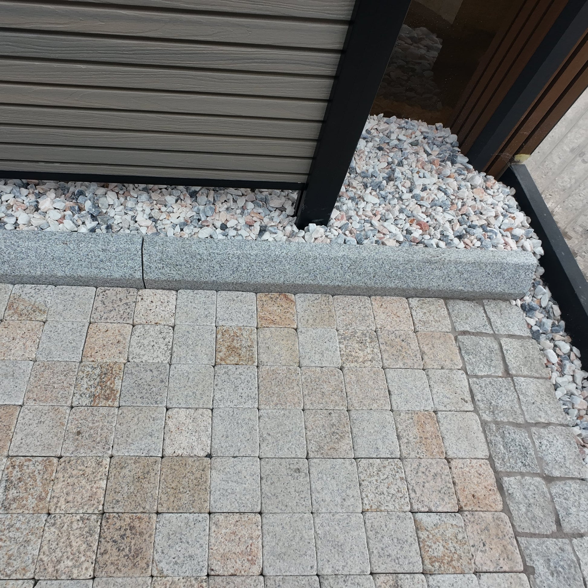 Paved area with stone tiles and gravel, featuring a building structure.