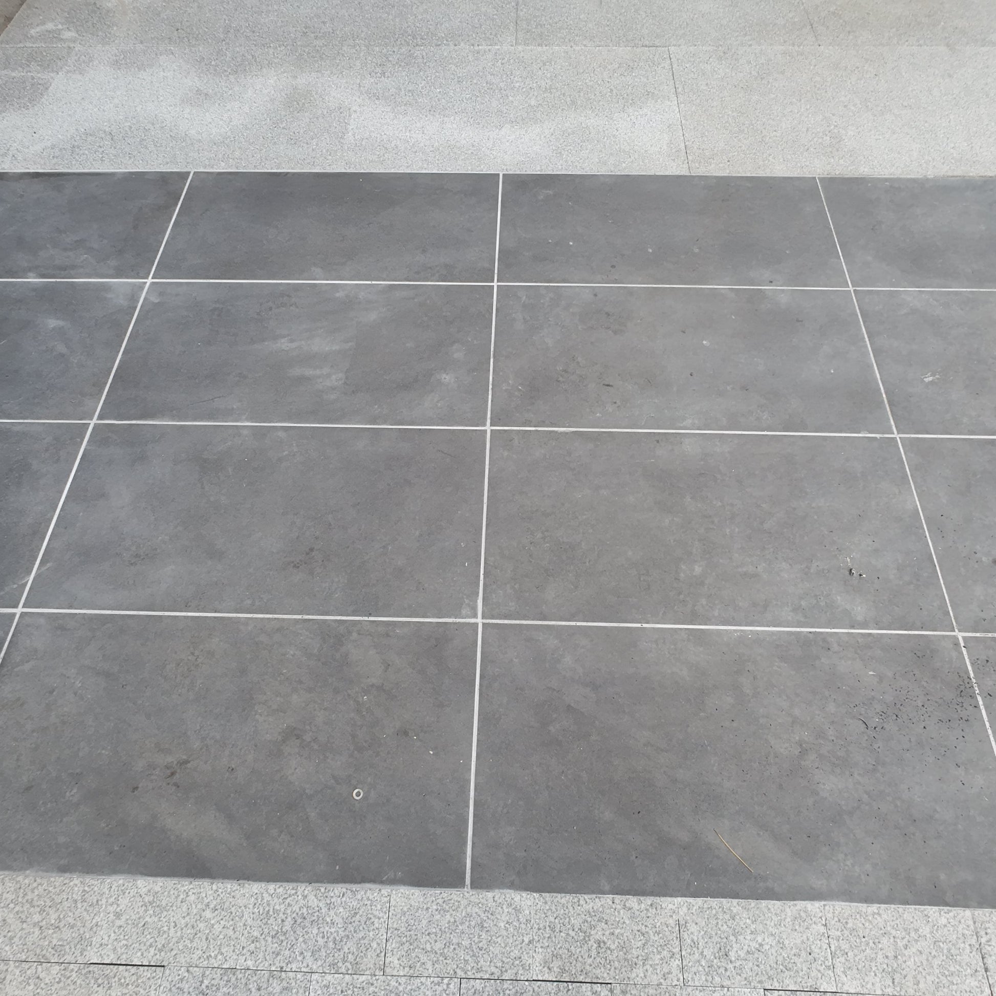 Gray tiled floor with a corner showing a step and wall.