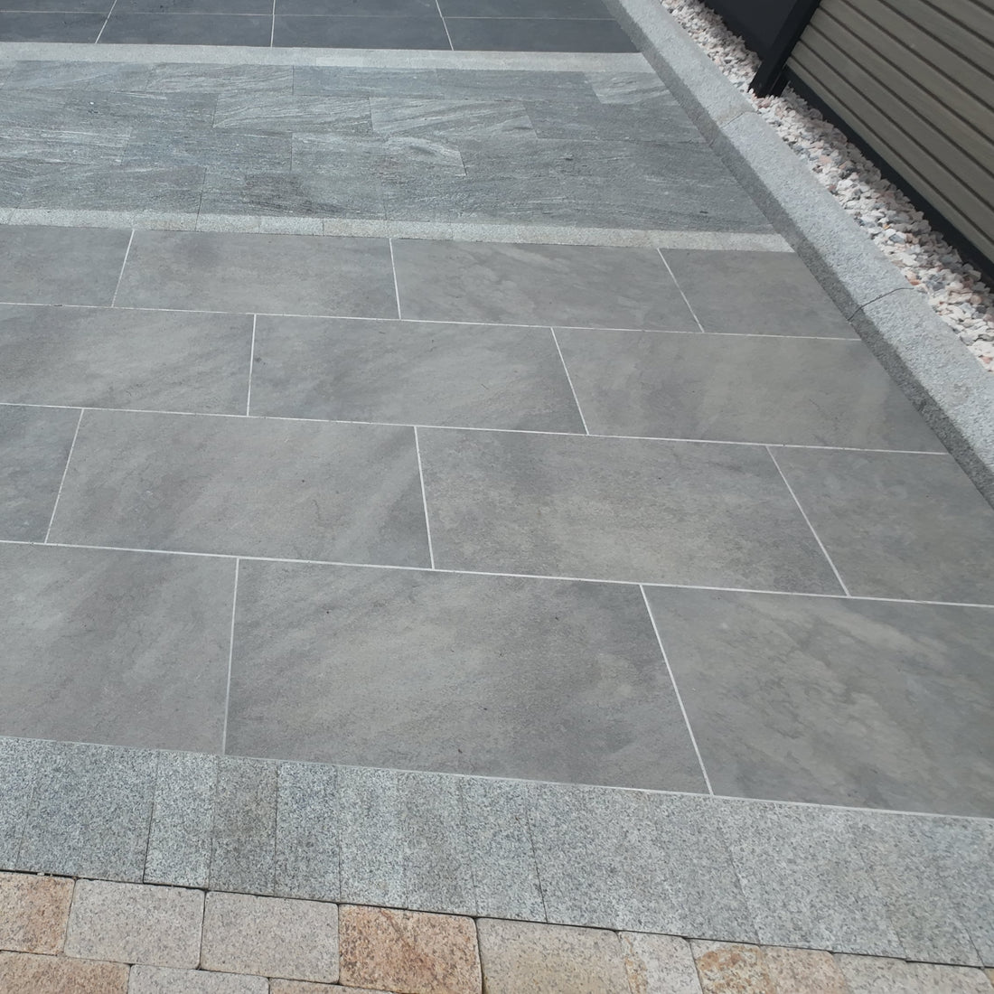Gray stone tiles on a patio with a small section of pebbles.