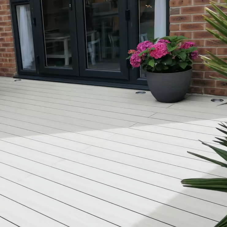 White wooden deck with a potted plant and a brick wall background